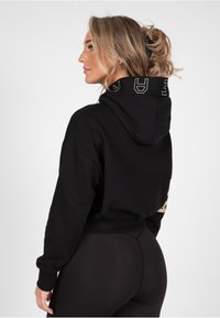 Sudadera negra con un acabado texturizado, que presenta un logo en la parte posterior y una capucha. Combinada con leggings negros ajustados.