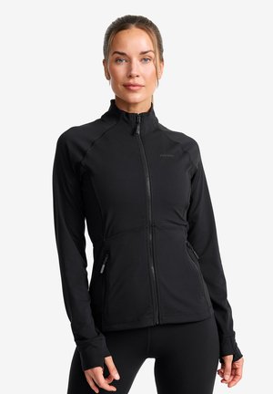 Black athletic jacket with a high collar, zippered front, and side pockets. Features flatlock seams and a fitted design.