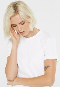 White cotton t-shirt with short sleeves, round neckline, and a smooth texture. A butterfly tattoo is visible on the arm.
