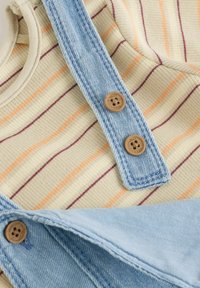 Chemise rayée aux couleurs claires, dotée d'une salopette en denim et de boutons en bois, présentant un design vestimentaire ludique et décontracté.