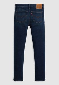 Jean en denim bleu foncé avec jambes droites, comportant deux poches arrière, des coutures contrastées et une étiquette en cuir beige sur la ceinture.