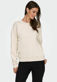 Heledbeez sweatshirt rundade kaeluse ja pehme tekstuuriga, vasakul õlal kaunistavad rhinestone'id. Kombineeritud mustade pükstega.