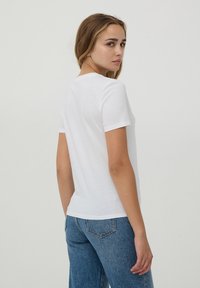 T-shirt bianco in cotone con maniche corte, collo rotondo e vestibilità rilassata, abbinato a jeans in denim blu. Tessuto morbido, senza fantasie.