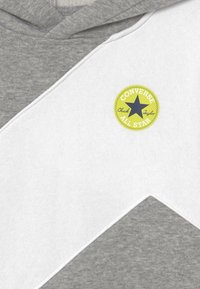 Felpa grigia e bianca con un design a chevron curvo, realizzata in morbido materiale. Include un'etichetta circolare gialla con "Converse All Star."