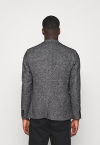 Grijze tweed blazer met een gestructureerd ontwerp, enkele achterventilatie en zwarte knopen op de mouwen. Geverfd materiaal met een subtiel patroon.