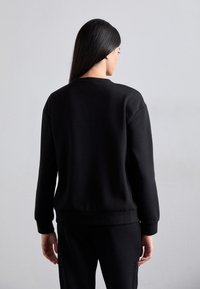 Felpa nera con maniche lunghe, collo rotondo e polsini a coste. Tessuto liscio e vestibilità morbida, abbinata a pantaloni coordinati.