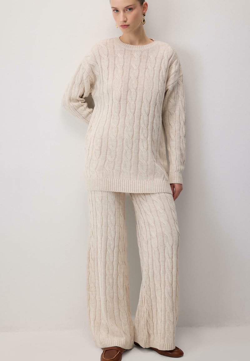 Kermainen neulepaita ja leveälahkeiset housut, joissa on nappineulekuvio. Teksturoidut kankaat, joissa on ribbireunat hihansuissa ja helmassa. Yksinkertainen muotoilu.