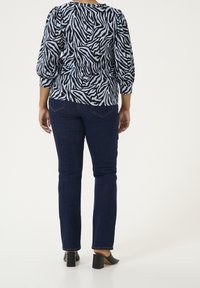 Blue and black zebra-patterned blouse with puff sleeves, paired with dark blue straight-leg jeans and black block-heeled mules.