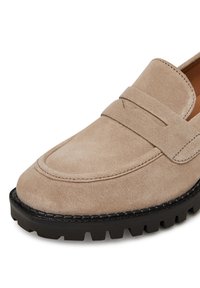 Béžové semišové mokasíny s prešitým dizajnom a hrubou čiernou gumovou podrážkou s protišmykovými drážkami. Klasický otvor na penny na hornej časti.
