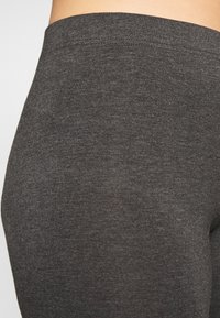 Mörkt grå tights i mjukt material med en slät yta och en bred elastisk midjeband. Närbild som framhäver tygdetaljer.