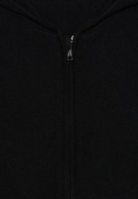Haut à capuche zippé noir en tissu doux et texturé. Il présente une fermeture éclair centrale et une capuche avec des détails côtelés le long des bords.
