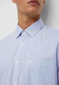 Camicia a quadri blu chiaro in cotone. Presenta un colletto button-down, una tasca frontale e un discreto dettaglio del logo sul petto.