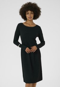 Melnā ribota kleita ar apaļu dekoltē, garām piedurknēm un teksturētu apakšējo daļu, kas piedāvā smalku detaļu uz piedurknēm.