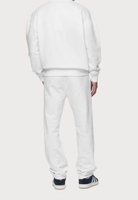 Bílá bavlněná mikina s kleslými rameny a žebrovanými manžetami, spárovaná s odpovídajícími bílými tepláky s elastickým pasem a jemnou texturou.