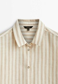 Chemise beige et blanche à rayures verticales, boutonnée, avec col pointu, en tissu léger en lin.