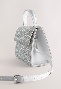 Bolso de mano plateado con un exterior de pedrería brillante, tapa superior plana y asa corta; incluye una correa desmontable y un interior liso.