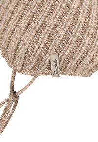 Beige knitted baby bonnet with ribbed texture and adjustable ties, featuring a small fabric label with brand name.