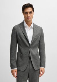 Gray wool blazer with a tailored fit, notch lapels, two front pockets, and two buttons. Worn over a white shirt with a crisp collar.