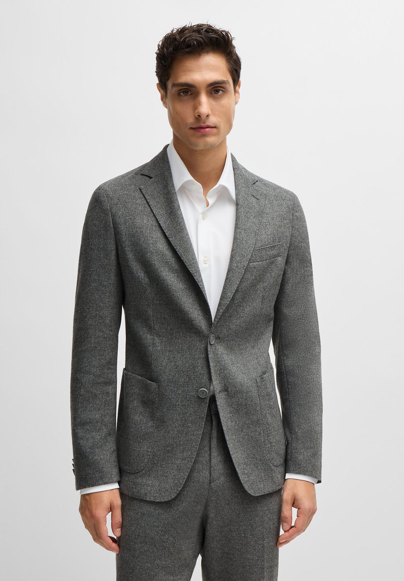 Gray wool blazer with a tailored fit, notch lapels, two front pockets, and two buttons. Worn over a white shirt with a crisp collar.