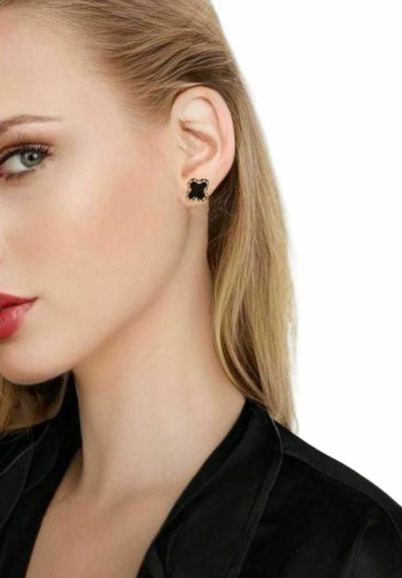 Svarta örhängen med guldfärgade accenter och en vågig design, mot en jämn yta, bärs av en modell.