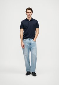 Námořnická polo košile s límečkem, v kombinaci se světle modrými džíny rovného střihu a černými mokasíny. Jednoduchý, čistý design s minimálními detaily.