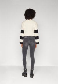 Cream and black striped ribbed sweater, gray fitted jeans, and black ankle boots. Sweater features long sleeves. Smooth texture throughout.