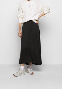 Jupe noire midi au design fluide, associée à un pull texturé blanc et à des baskets gris clair. Tissu lisse avec un léger éclat.
