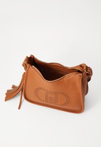Borsa a tracolla in pelle marrone con finitura texture, chiusura con zip e motivo decorativo a ritaglio. Presenta un accento con pompon e tracolla regolabile.
