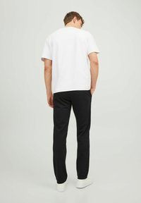 T-shirt bianco a maniche corte abbinato a pantaloni neri, mostrato di spalle. Il modello indossa sneakers bianche; tessuto morbido con una vestibilità casual.