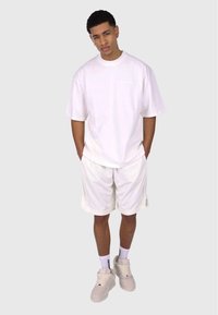 Hvid oversized T-shirt, matchende hvide shorts, beige sneakers og hvide sokker. Materiale i bomuldsblanding med en afslappet pasform og minimale detaljer.
