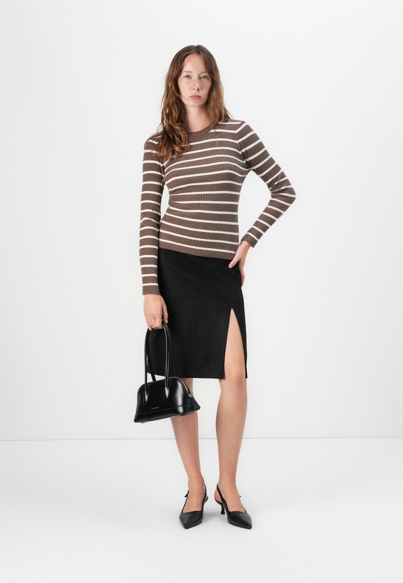 Gestreiftes, braun- und weißes, geripptes Langarmoberteil, schwarzer Rock mit hohem Schlitz, schwarze Handtasche und spitze schwarze Absätze, vor einem schlichten weißen Hintergrund.