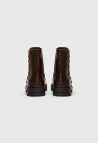 Botas de tobillo de cuero marrón con un acabado suave, puntera redonda, paneles laterales elásticos y suelas negras gruesas. Acento bordado notable en los lados.