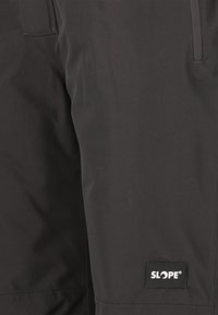 Svarta snöbyxor gjorda av slitstark material, med en ficka med dragkedja och en synlig logotypetikett. Slät textur med en elegant design.