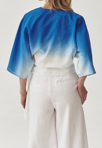Kimono azul degradado con mangas amplias, tejido ligero, que pasa de un azul profundo a blanco, emparejado con pantalones blancos holgados.