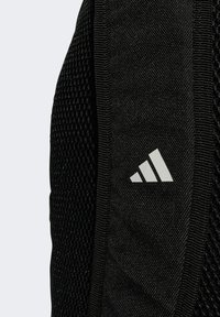 Nahaufnahme eines schwarzen, strukturierten Stoffes mit dem weißen Adidas-Logo auf einem gepolsterten Riemen, der atmungsaktives Mesh-Material aufweist.