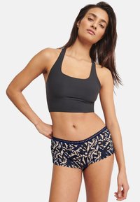 Sort cropped sports-bh med brede stropper, kombineret med mønstrede navy- og beige boyshorts med en tekstureret linning.