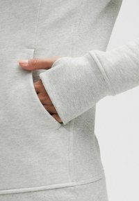 Lys grå sweatshirt med fokus på en sidelomme, ribbede manchetter og en glat tekstur. Har en tætsiddende pasform og diskrete sømme.