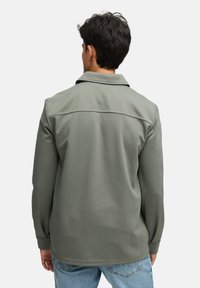 Grå struktureret jakke med krave, lange ærmer og rygindsatsdetalje. Kombineret med lyseblå jeans.