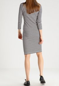 Robe rayée à manches trois-quarts, motif noir et blanc, silhouette ajustée, longueur genoux, associée à des chaussures noires.