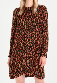Robe à manches longues avec un imprimé léopard dans des couleurs vert, rouge et noir. Caractéristiques d'une coupe loose et d'un tissu doux pour le confort.