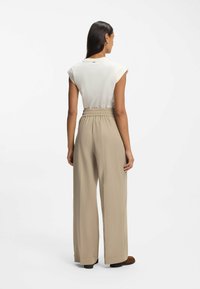 Ivoorkleurig topje met korte mouwen en opgerolde manchetten, gecombineerd met beige broek met hoge taille en wijde pijpen, voorzien van een gerimpelde elastische tailleband.