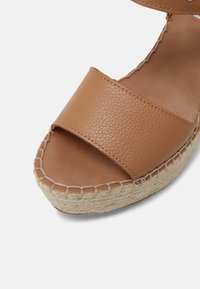 Sandale espadrille en cuir marron clair à bout ouvert avec semelle plateforme en jute cousue et bride de cheville visible sur fond blanc.