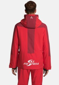 Rote Skijacke mit Kapuze, ausgestattet mit einem Farbblock-Design in dunkleren Tönen, Logo auf der Rückseite und glattem, strukturiertem Stoff.