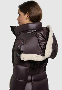 Brun puffjacka med en avtagbar krämfärgad fleecekrage. Har dragkedje- och knappstängning, kviltad design och en åtdragen midja.