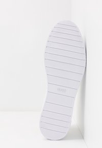 Sole di sneaker bianca in gomma testurizzata, caratterizzata da scanalature orizzontali e un motivo circolare nella punta. Logo "HUGO BOSS" vicino al tallone.