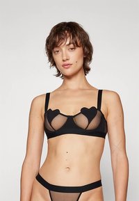 Schwarzes Bralette mit herzförmigen Aussparungen, durchscheinendem Material, breiten Trägern und einem glatten Bund. Dazu passt ein schwarzer, passender Tanga.