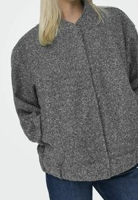 Chaqueta gris texturizada con un corte relajado, que presenta un cuello alto y cierre frontal, hecha de una tela suave y acogedora.