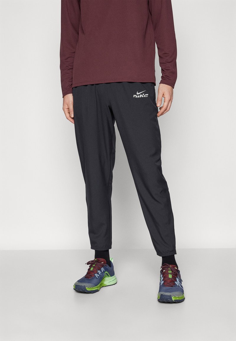 Zwarte trainingsbroek van Nike met elastische boorden, gecombineerd met multicolore sportschoenen met groene accenten en gestructureerde blauwe stof.
