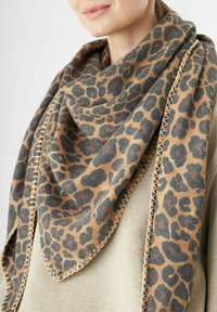 Écharpe en imprimé léopard dans des tons beige et marron, présentant une forme triangulaire et une finition texturée. Bordée d'un détail de couture contrasté.