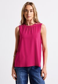 Top senza maniche fucsia realizzato in tessuto liscio, con scollatura arricciata e vestibilità morbida. Indossato con jeans in denim blu.